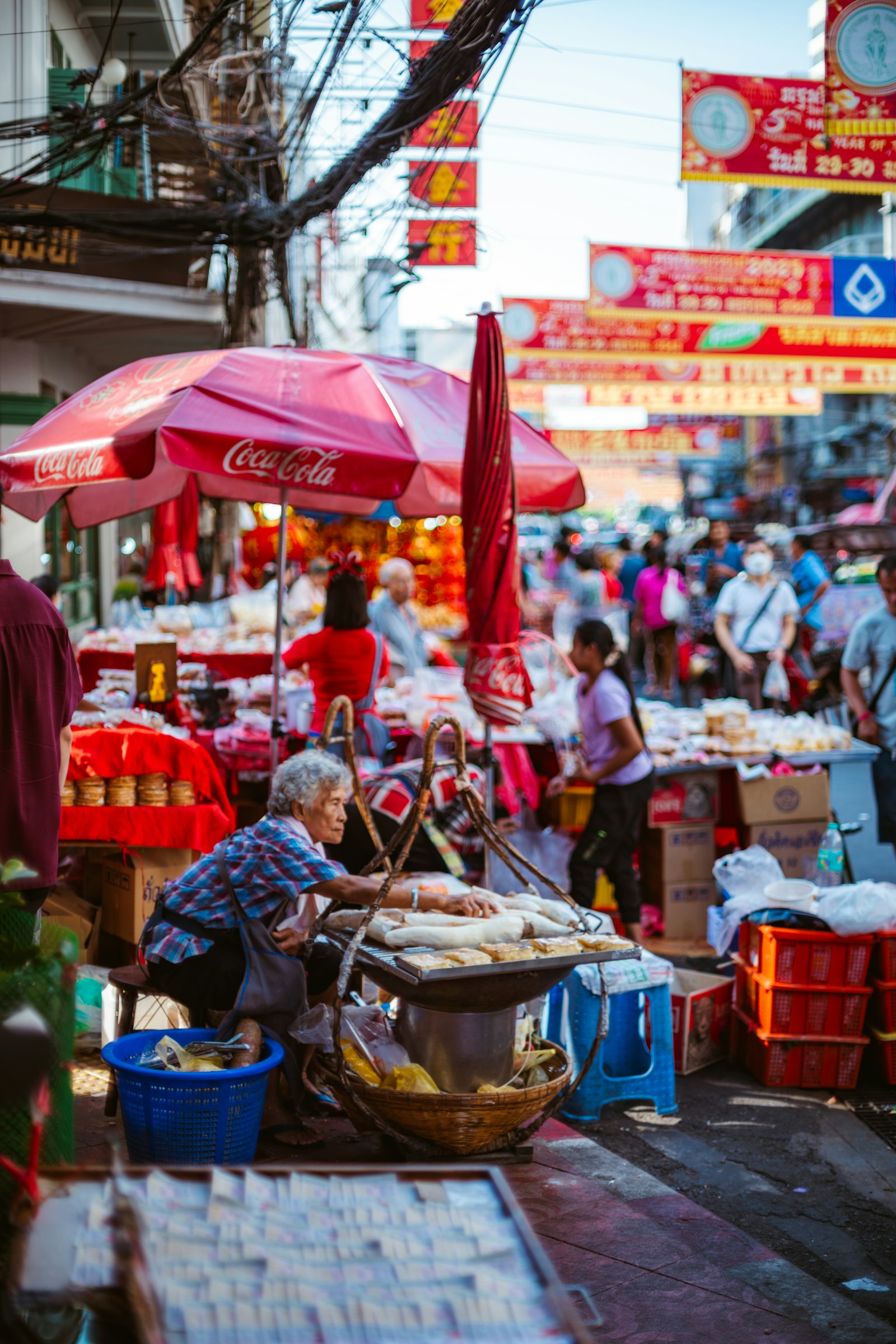 A bustling city street market with vendor umbrellas and lanterns overhead